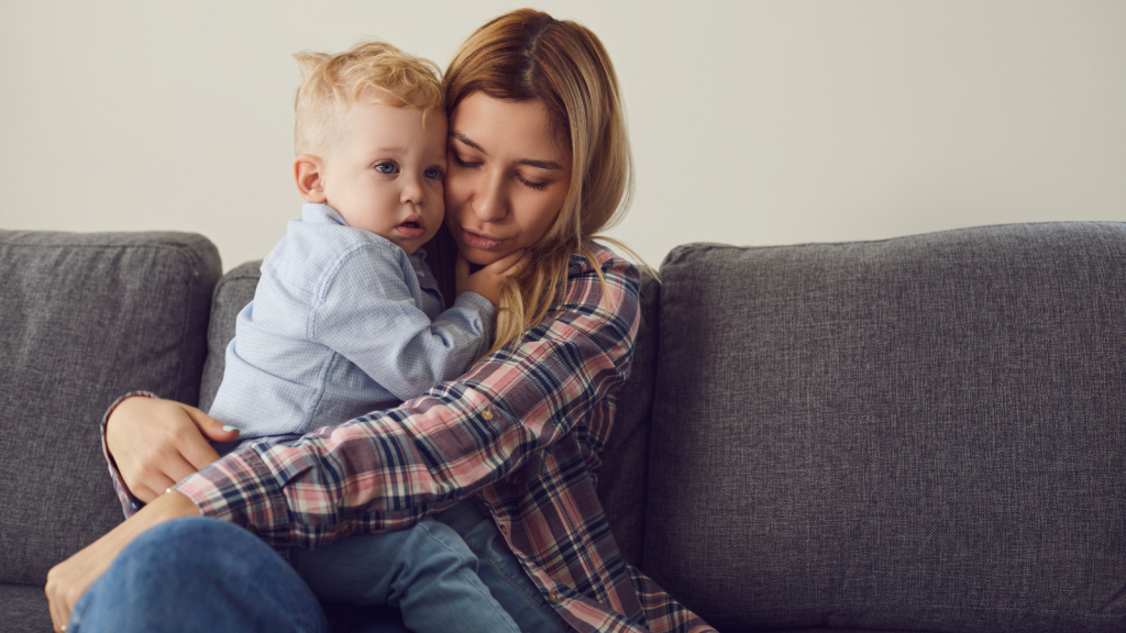 A mother is holding her baby tight in her arms, sitting on a couch